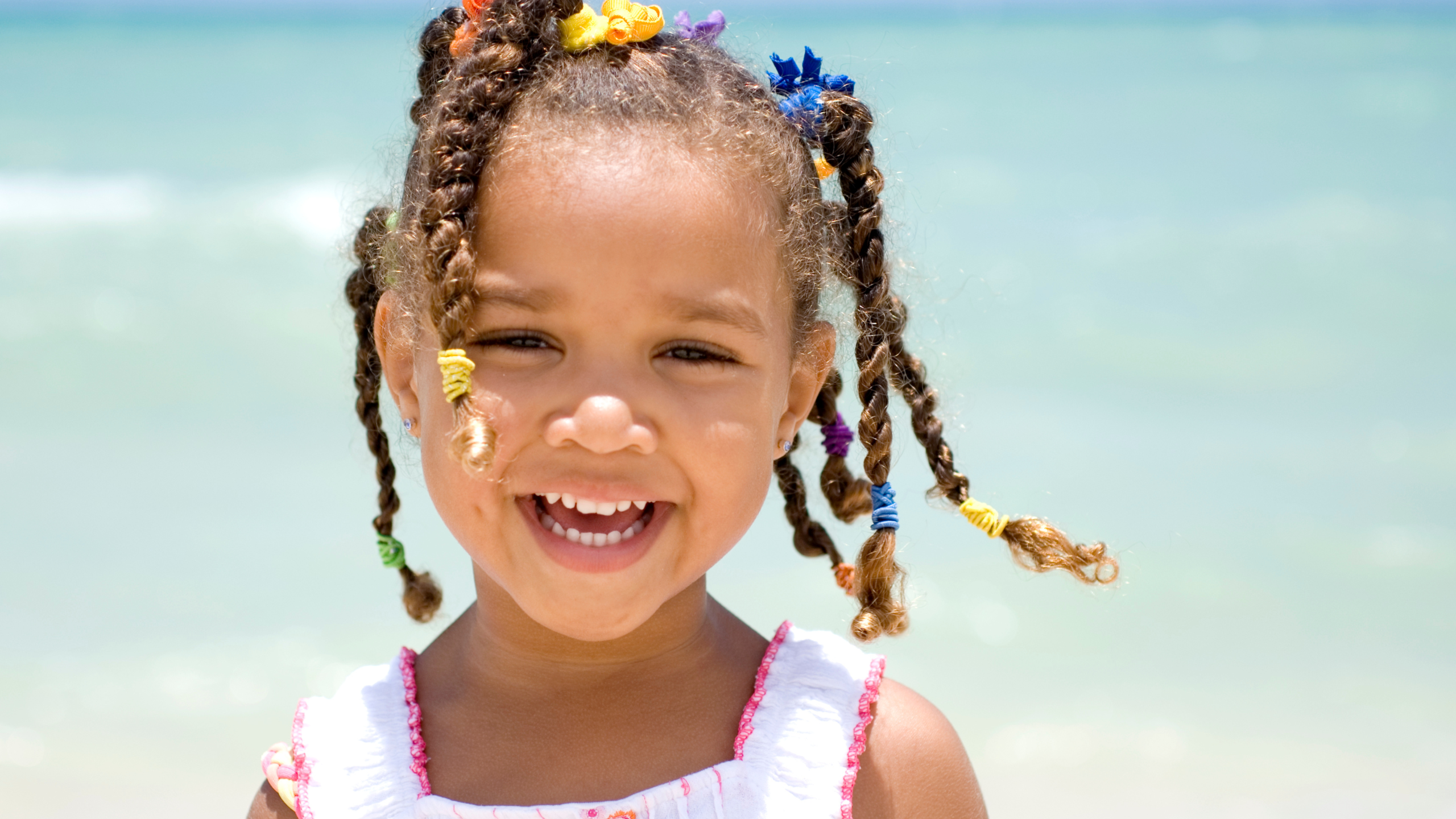 A little girl smiling with the beach as the background.