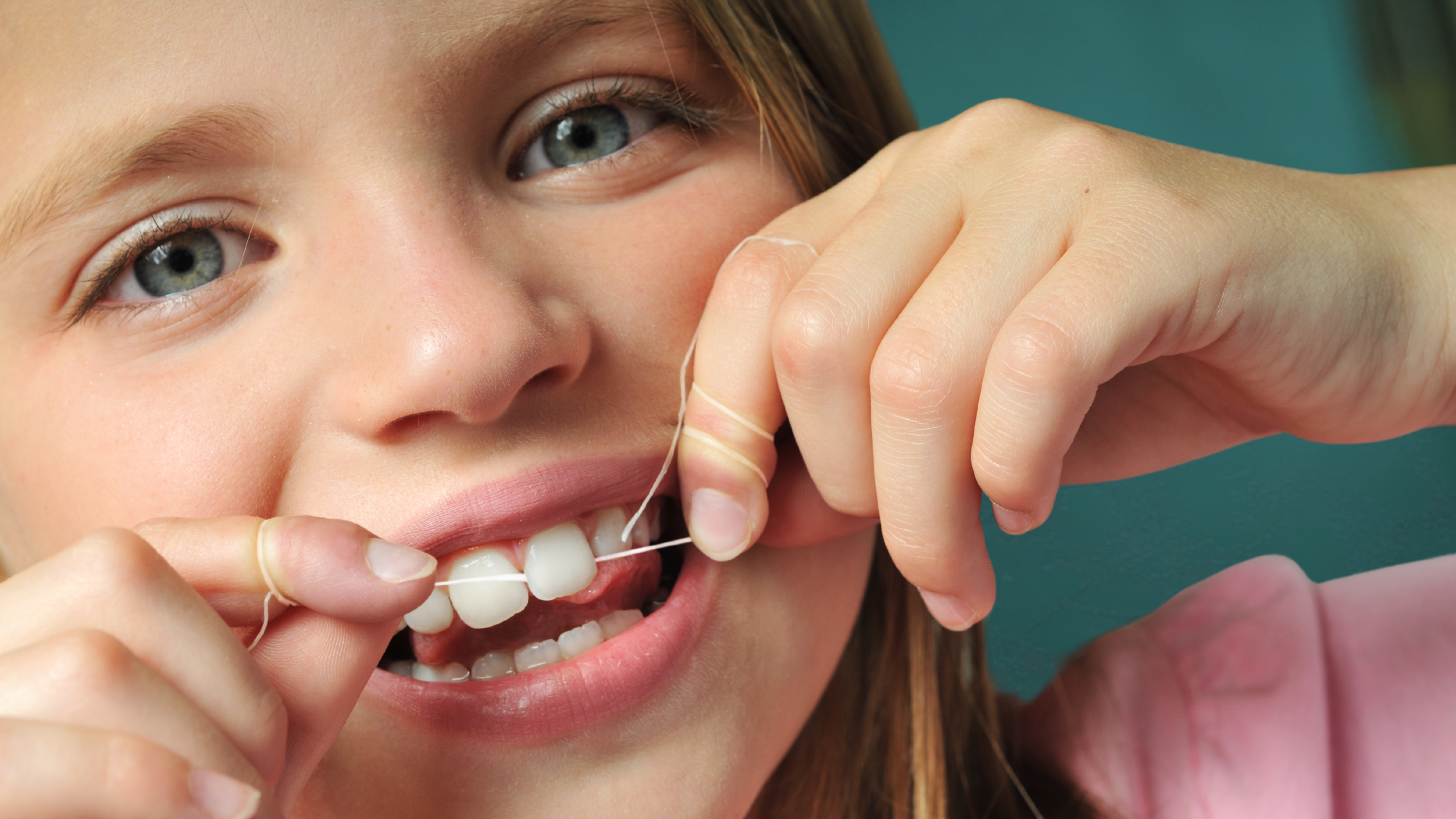 A close up photo of a little girl flossing her teeth.